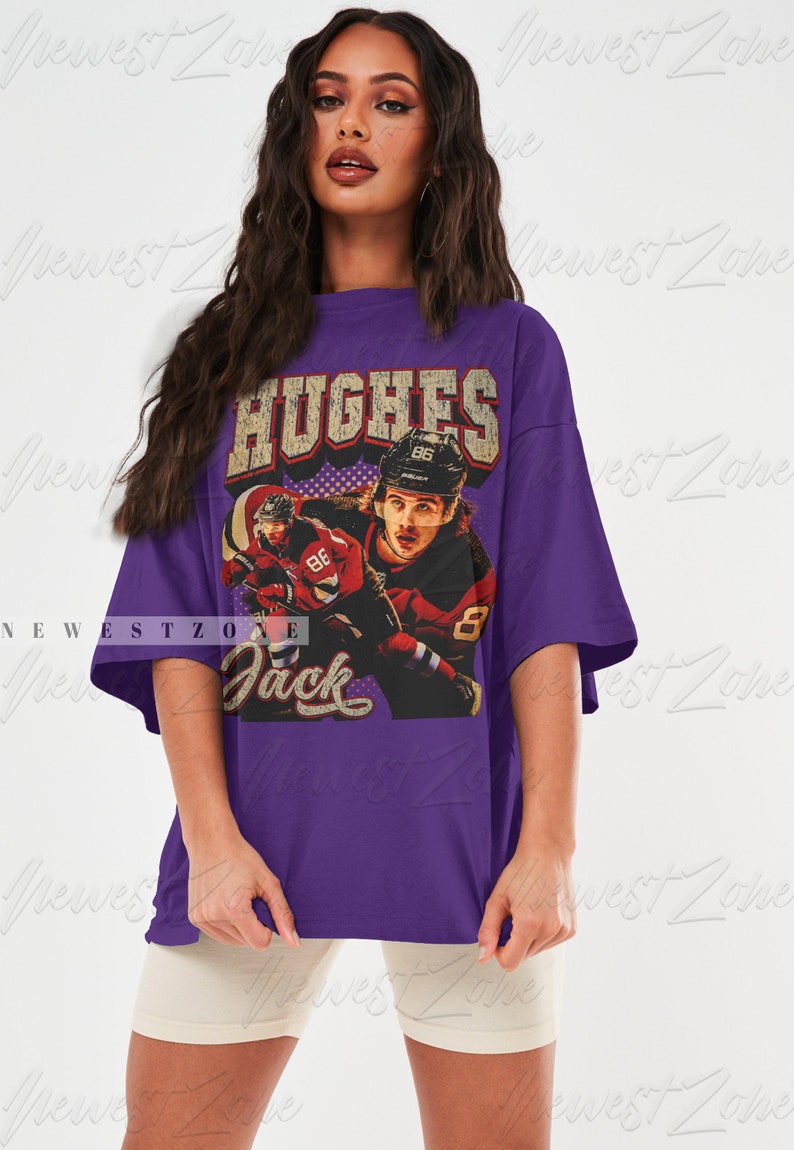 May include: Purple oversized t-shirt with a vintage graphic of a hockey player wearing a red and black jersey with the text "HUGHES 86" on the back of the jersey. The text "Jack" is printed below the graphic.