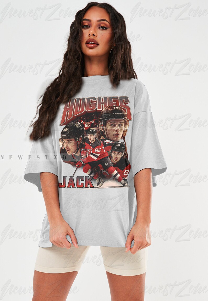 Puede incluir: Una camiseta gris de gran tama&ntilde;o con un gr&aacute;fico de estilo vintage de jugadores de hockey. El gr&aacute;fico presenta el texto "HUGHES" y "JACK" y el n&uacute;mero "86".