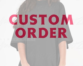 Op de afbeelding: Een zwart, oversized t-shirt met de woorden "CUSTOM ORDER" in rode blokletters op de voorkant. Het shirt heeft korte mouwen en een losse pasvorm. De achtergrond is wazig.