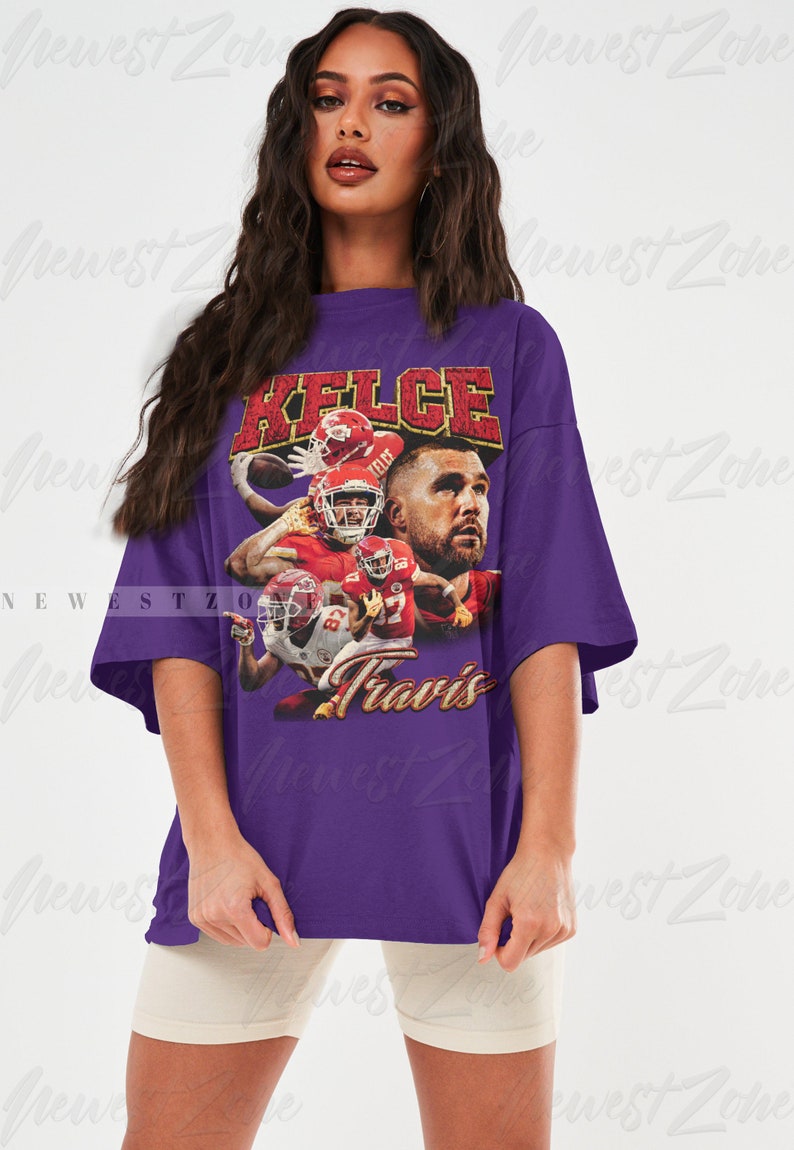 May include: Purple oversized t-shirt with a vintage-style graphic of a football player wearing a red jersey with the name "Kelce" and the number "87" on it. The text "Travis" is printed below the graphic.