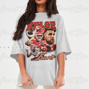 May include: A gray oversized t-shirt with a vintage-style graphic of a football player wearing a red and white jersey. The graphic includes the text "Kelce" and "Travis".