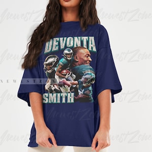 May include: Navy blue t-shirt featuring a graphic of Devonta Smith, with the text "DEVONTA SMITH" in distressed white lettering. The graphic includes images of the football player in action. The shirt is a relaxed fit.