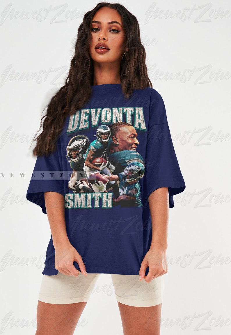 May include: Navy blue t-shirt featuring a graphic of Devonta Smith, with the text "DEVONTA SMITH" in distressed white lettering. The graphic includes images of the football player in action. The shirt is a relaxed fit.