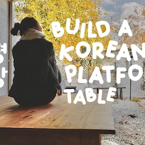 May include: A wooden platform table with the text "BUILD A KOREAN PLATFORM TABLE" in white. The image shows a person sitting on the table, with a backdrop of trees and a fence.