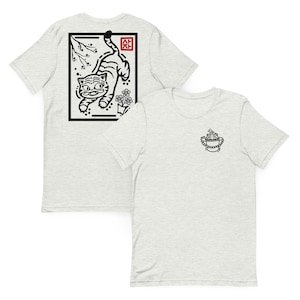 May include: Two light gray t-shirts. One features a black and white illustration of a tiger within a black rectangular frame. The other shirt has a small black and white graphic of a bird in a bucket.