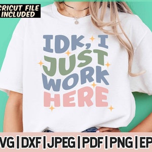 May include: White t-shirt with a graphic design that says "IDK, I JUST WORK HERE" in colorful, stylized lettering.