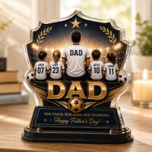 May include: A decorative acrylic Father's Day gift featuring a soccer theme. The design includes a father figure with four children, each wearing a jersey with a name and number. The text "DAD" is prominently displayed, along with the message "Happy Father's Day!"