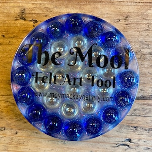 May include: A blue and white round felt art tool with the text "The Mool Felt Art Tool" and the website "www.moymackaygallery.com".