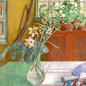 May include: A clear glass vase filled with white daffodils and green pine branches sits on a green tablecloth. The vase is in front of a yellow wall with a wooden cabinet and a window with green plants in pots.