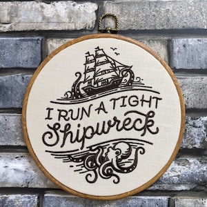 May include: Embroidered hoop art with a brown ship and tentacles, and the text "I run a tight shipwreck".
