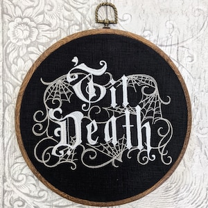 May include: A black embroidery hoop with a white embroidered design that says "Till Death" with a spiderweb pattern around the words.