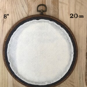 Puede incluir: Un aro de bordado de madera de 20 cm de di&aacute;metro con un inserto de fieltro blanco. El aro tiene un anillo de lat&oacute;n en la parte superior para colgarlo.