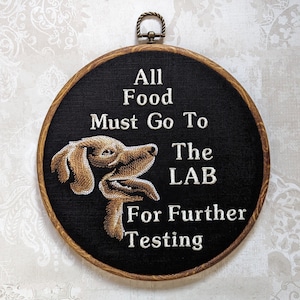 May include: A black and brown embroidery hoop with the text "All Food Must Go To The LAB For Further Testing" and a brown dog illustration.