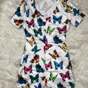 Könnte beinhalten: Weißer, kurzärmeliger Einteiler-Pyjama mit einem bunten Schmetterlingsmuster.