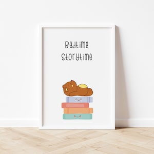 Puede incluir: Una impresión enmarcada en blanco con el texto "Bedtime Storytime" y un oso marrón de dibujos animados acostado sobre una pila de libros coloridos con caras felices.