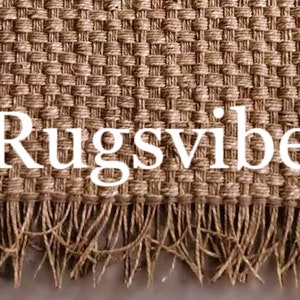 May include: A close-up of a natural fiber rug with a woven texture and fringe. The rug is light brown in color and has the text "Rugsvibe" printed on it.