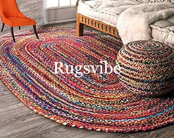 May include: An oval-shaped braided rug and a matching round pouf ottoman, both crafted from multicolored fabric strips in vibrant shades of red, blue, yellow, and green. The text Rugsvibe is centered on the rug in white, sans-serif lettering.