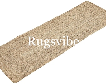 May include: A natural fiber runner rug made from jute. The rug has a woven texture and a light brown color. The rug is rectangular and has a fringed edge. The rug is labeled "Rugsvibe".