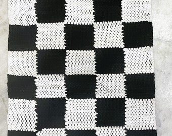 May include: Black and white checkered rug with fringe on all sides. The rug is made of a woven material and has a geometric pattern.