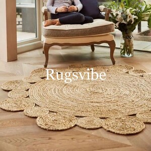 May include: A round, natural fibre rug with a circular design. The rug has a woven texture and a scalloped edge. The rug is light brown in colour and is placed on a wooden floor.