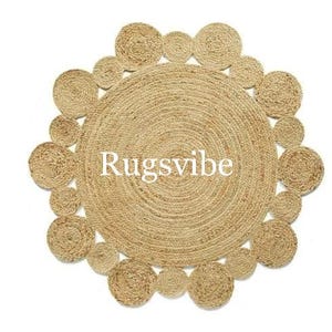 May include: A round, natural fibre rug with a circular pattern of woven jute. The rug has a natural, beige colour and a textured surface. The text "Rugsvibe" is printed in white on the rug.