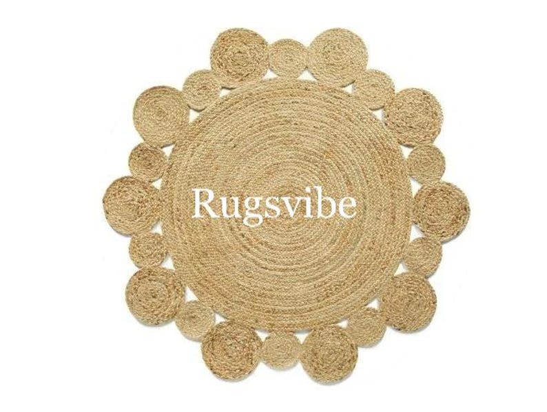 May include: A round, natural fibre rug with a circular pattern of woven jute. The rug has a natural, beige colour and a textured surface. The text "Rugsvibe" is printed in white on the rug.