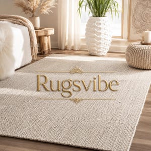 May include: A rectangular area rug with a thick, woven, light beige texture. The rug features a consistent, dense loop pile construction. Centered on the rug is the gold-colored text "Rugsvibe" flanked by two decorative horizontal lines.