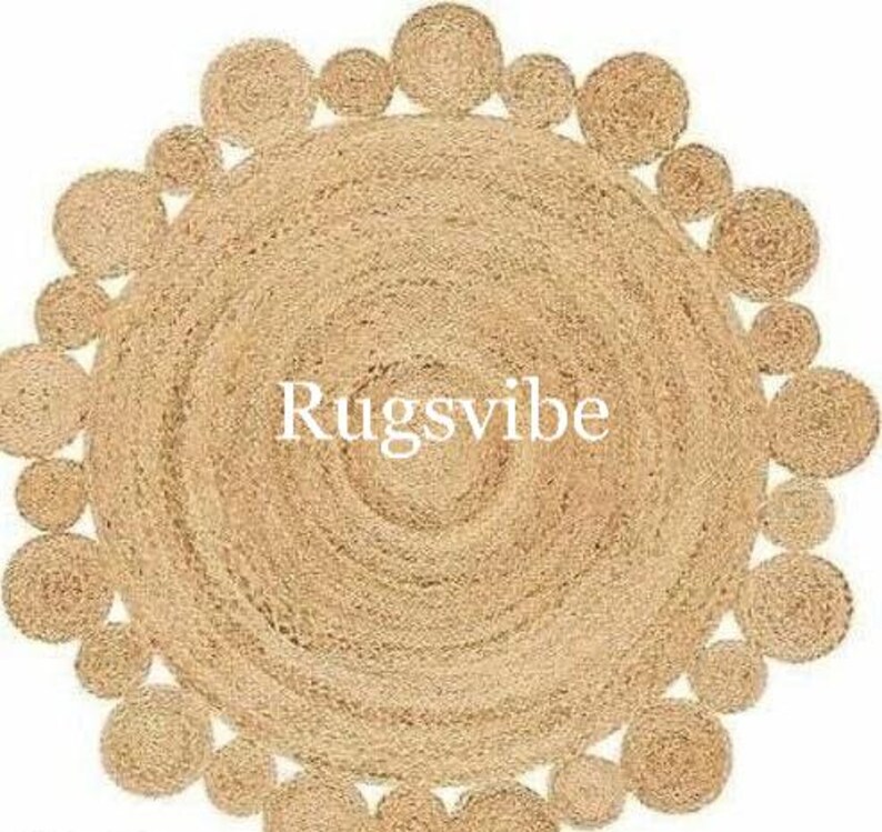 May include: A round jute rug in a natural beige colour. The rug has a circular pattern of woven jute rope around the edge. The centre of the rug is a solid beige colour. The text "Rugsvibe" is printed in the centre of the rug.