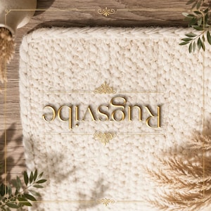 May include: A rectangular off-white chunky knit rug with a thick braided border. The word Rugsvibe is printed in gold lettering across the center, flanked by two decorative gold filigree flourishes within a thin gold rectangular frame.