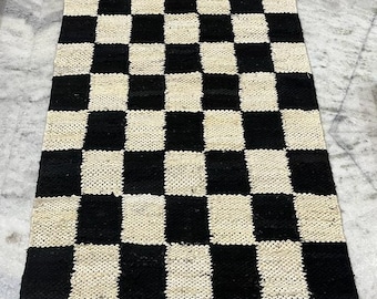 May include: Black and white checkered rug with fringe. The rug is made of woven material and has a geometric pattern.