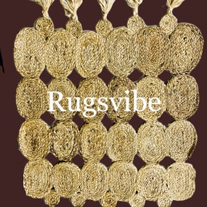 Puede incluir: Una alfombra de fibra natural con un patrón circular y flecos. La alfombra está hecha de yute y tiene un color beige natural. El texto "Rugsvibe" está impreso en la alfombra.