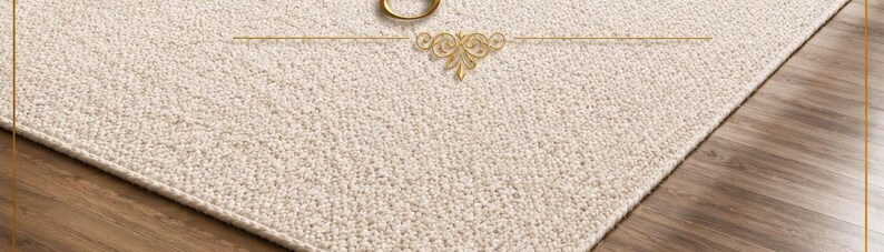 May include: A rectangular area rug with a textured, off-white surface. The rug features a gold-colored circular ring centered at the top edge, accompanied by a decorative gold-colored filigree emblem positioned directly below the ring.