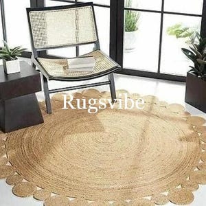 May include: A round jute rug with a scalloped edge. The rug is light brown and has a natural, rustic look. The rug is placed on a wooden floor and a chair is sitting on the rug.