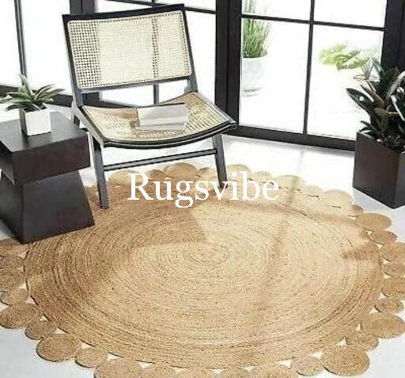 May include: A round jute rug with a scalloped edge. The rug is light brown and has a natural, rustic look. The rug is placed on a wooden floor and a chair is sitting on the rug.