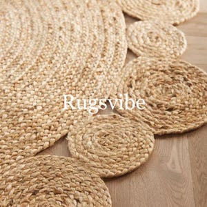 May include: A natural fibre rug with a circular design featuring a series of concentric circles in a light brown colour. The rug has a textured, woven appearance and is made of jute.