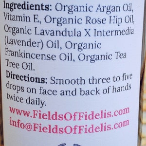 Pu&ograve; includere: Un'etichetta bianca con testo nero che descrive gli usi e gli ingredienti di un olio per il viso. L'etichetta include il nome del marchio "FieldsOfFidelis.com" e un indirizzo del sito web. L'etichetta &egrave; attaccata a una bottiglia di vetro trasparente.