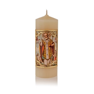 Pode incluir: Vela de pilar de cor marfim com uma faixa decorativa com uma imagem religiosa. A faixa tem um design de filigrana dourada. A imagem retrata um santo em vestes ornamentadas, segurando um báculo e um livro. Anjos também estão presentes.