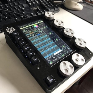 Puede incluir: Un panel de control negro con una pantalla táctil y varias perillas plateadas. La pantalla muestra una interfaz colorida con varias configuraciones. El panel tiene botones etiquetados y el texto "JEOS" es visible en las perillas.