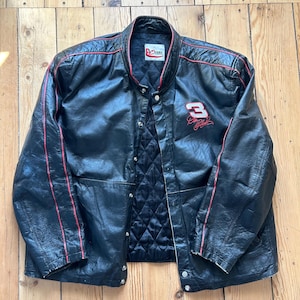 May include: Black leather jacket with red trim and the number "3" embroidered on the front. The jacket has a quilted lining and snap closures. The jacket is a vintage style.