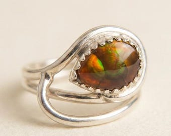 Op de afbeelding: Zilveren ring met een ovale edelsteen met rode, oranje en groene tinten. De edelsteen is gezet in een geschulpte zetting. De ring heeft een uniek, vloeiend ontwerp. Een opvallend sieraad.