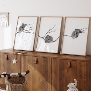 May include: Three framed prints of watercolor illustrations of koalas sleeping on branches. The prints are in a light wood frame and are hanging on a wall above a wooden cabinet.