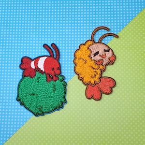 May include: Two embroidered iron-on patches. One is a red and white shrimp on a green bush. The other is a yellow and orange cartoon shrimp with a red tail.