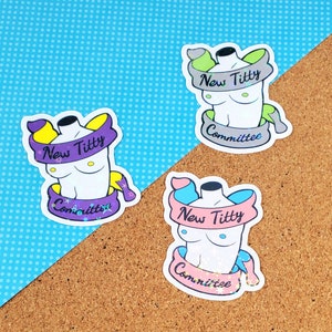 May include: Three colorful stickers with a cartoon image of a torso with the text "New Titty Committee" on each. The stickers are on a corkboard background.