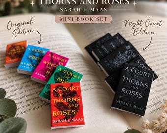 May include: A collection of miniature books titled A Court of Thorns and Roses by Sarah J. Maas, featuring an Original Edition set with colorful covers and a Night Court Edition set with black covers, all displayed on an open book page.