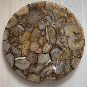 May include: A round agate coaster with a natural, polished finish. The coaster features a variety of brown, white, and beige agate slices, creating a unique and eye-catching design.