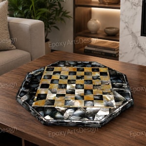May include: An octagonal chess board with a black and gold checkered playing surface. The board is framed with a mosaic of black, grey, and gold iridescent tiles. The board is displayed on a dark wood table.
