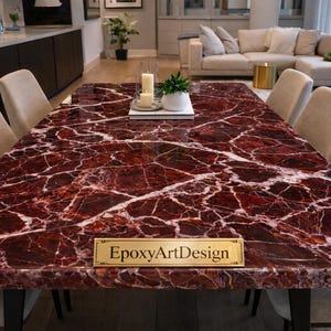 以下が含まれることがあります： 白い縞模様のある、深紅の大理石のような表面の長方形のダイニングテーブル。テーブルの周りにはベージュの椅子があり、キャンドルと小さな植物が置かれています。テーブルにはEpoxyArtDesignと書かれた金の看板があります。