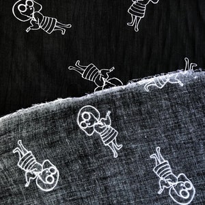 May include: Two pieces of black fabric with a white repeating pattern of a person with glasses and a striped dress. The fabric is textured and has a subtle sheen.