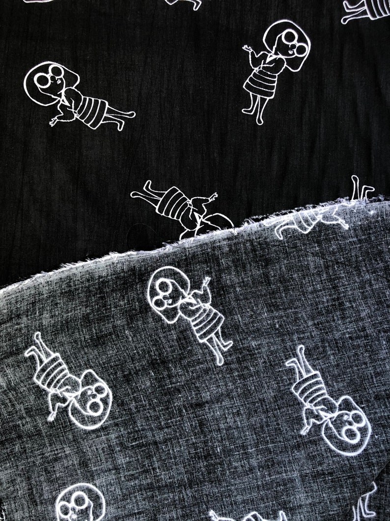May include: Two pieces of black fabric with a white repeating pattern of a person with glasses and a striped dress. The fabric is textured and has a subtle sheen.