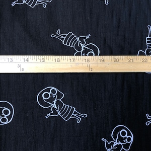 May include: Black fabric with a white repeating pattern of a stylized person with large round glasses. The fabric is measured with a wooden ruler.